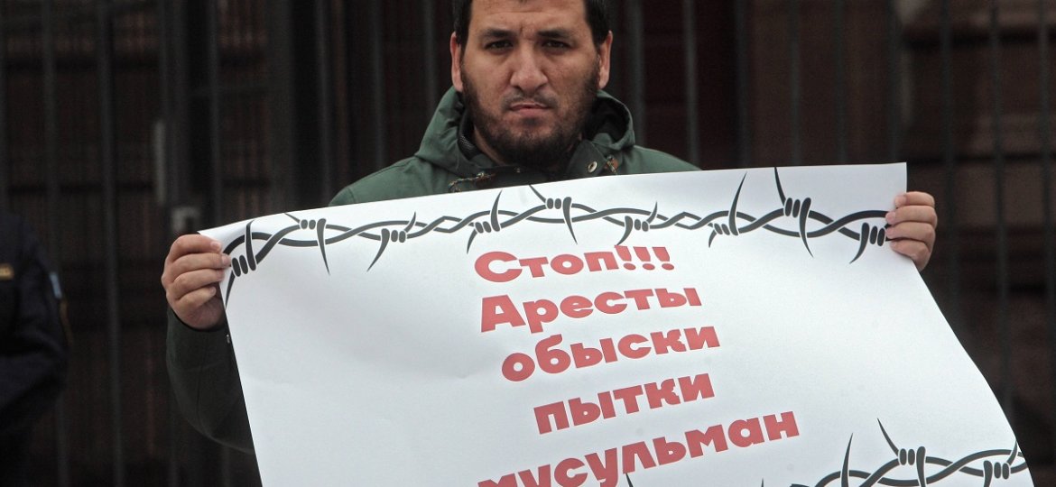 A man holds a placard calling to stop arrests house checks and tortures of Muslims during a protest